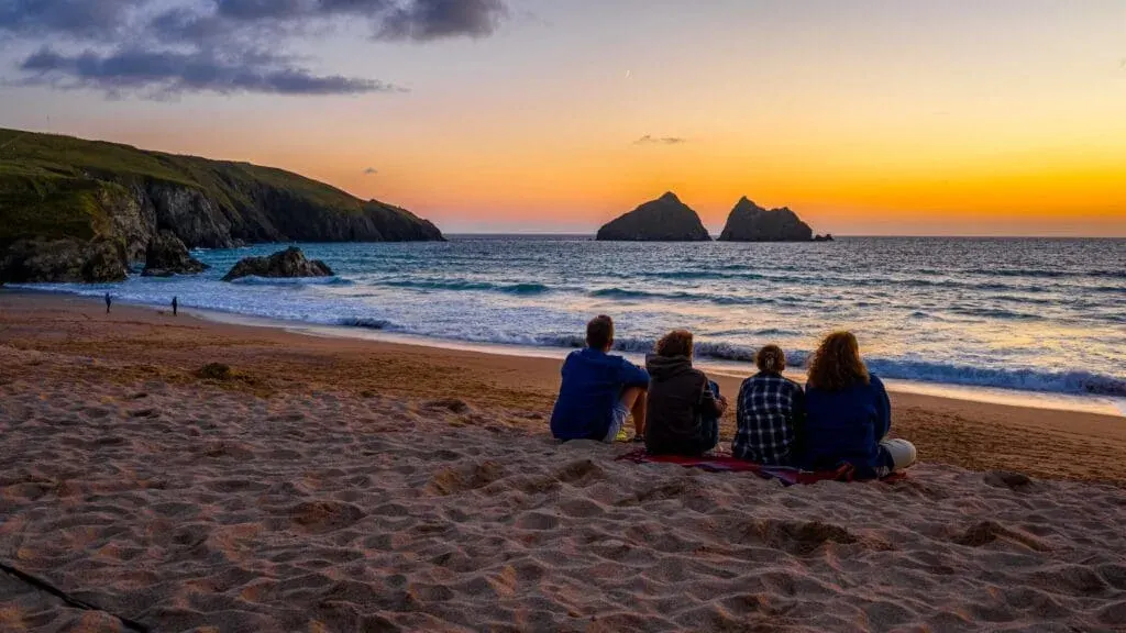 A group gathers to enjoy the sunset over the Gull Rocks at Holywell Bay Beach, Cornwall