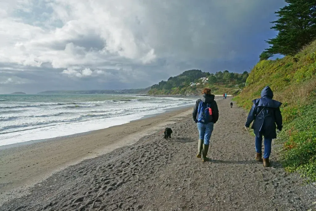 Walkers along the coastal footpath on Downderry Beach, Cornwall, on an overcast morning