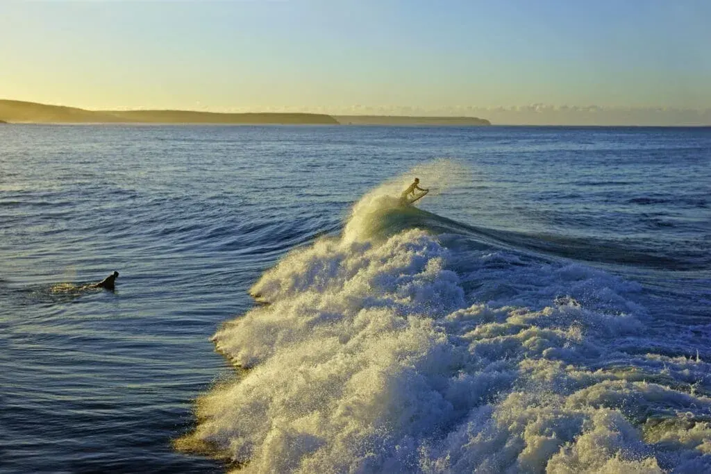 Surfers riding the waves at sunrise on the incoming tide at Porthleven Beach